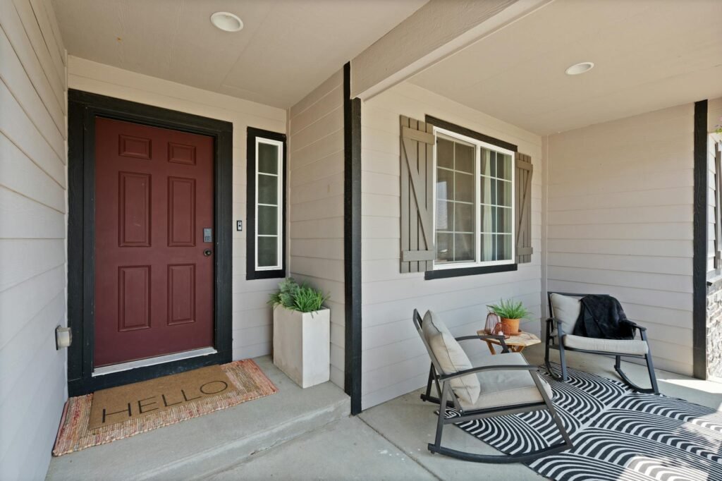A tidy front entry with a simple mat, clean door, and two potted plants.