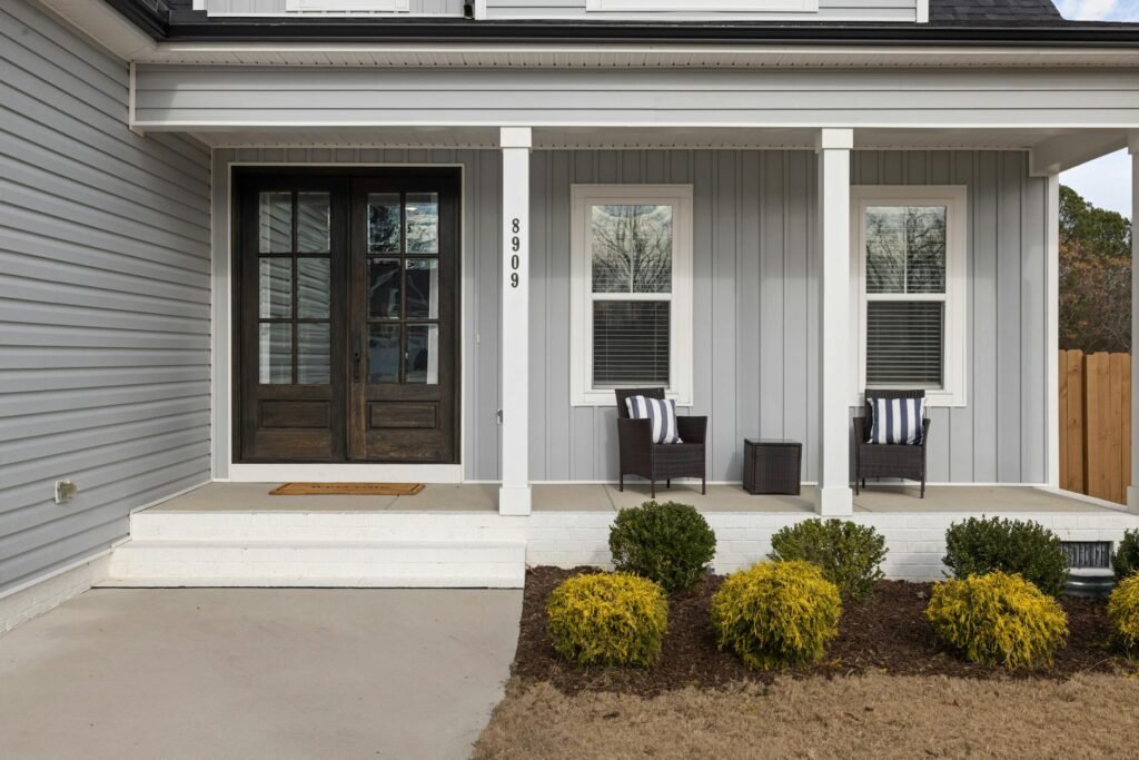 A clean front entry with a simple doormat and two potted plants.