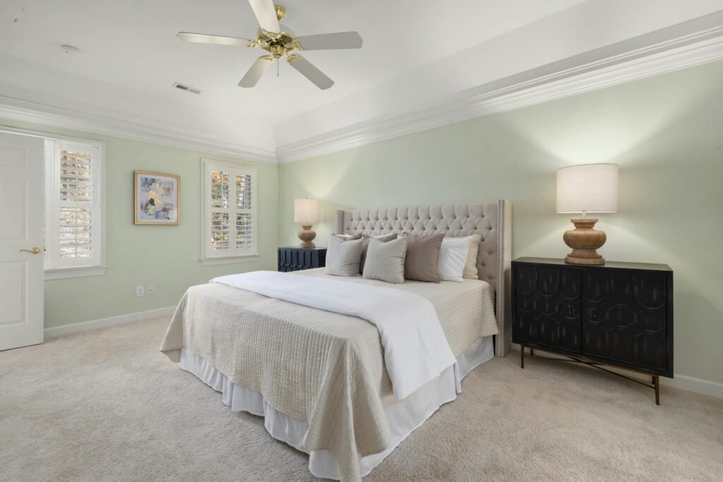 A small bedroom staged with a queen bed, low headboard, and compact nightstands.