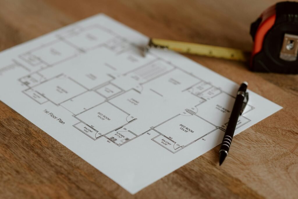 A desk with a tape measure, notebook, floor plan sketches, and a calculator