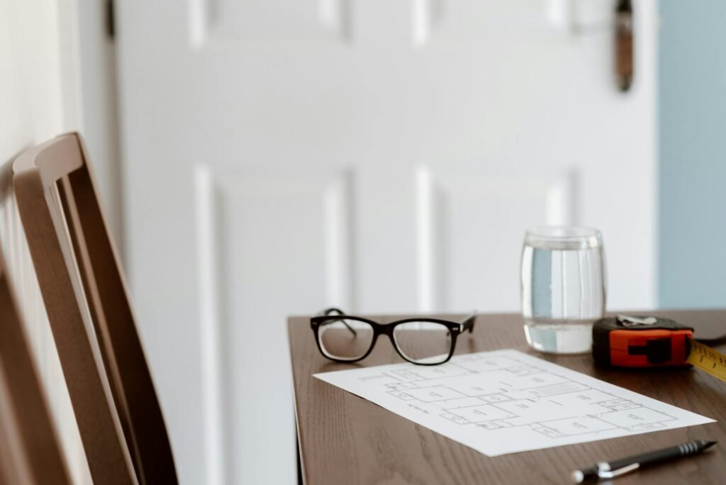 A desk with a floor plan, calculator, measuring tape, and notes for planning furniture size.