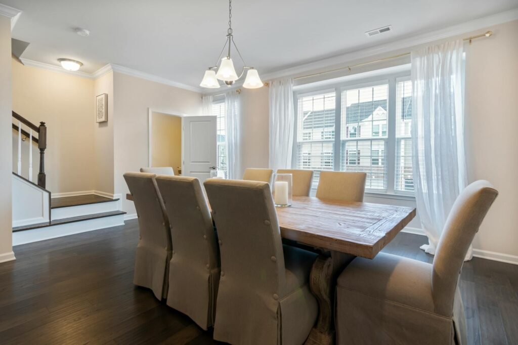 Dining room with warm overhead light, wood floor, and simple curtains